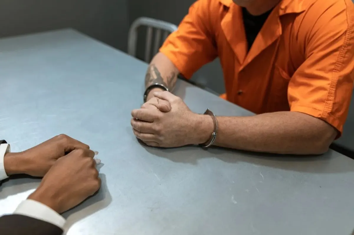 Client in a jail uniform meeting with a defense attorney